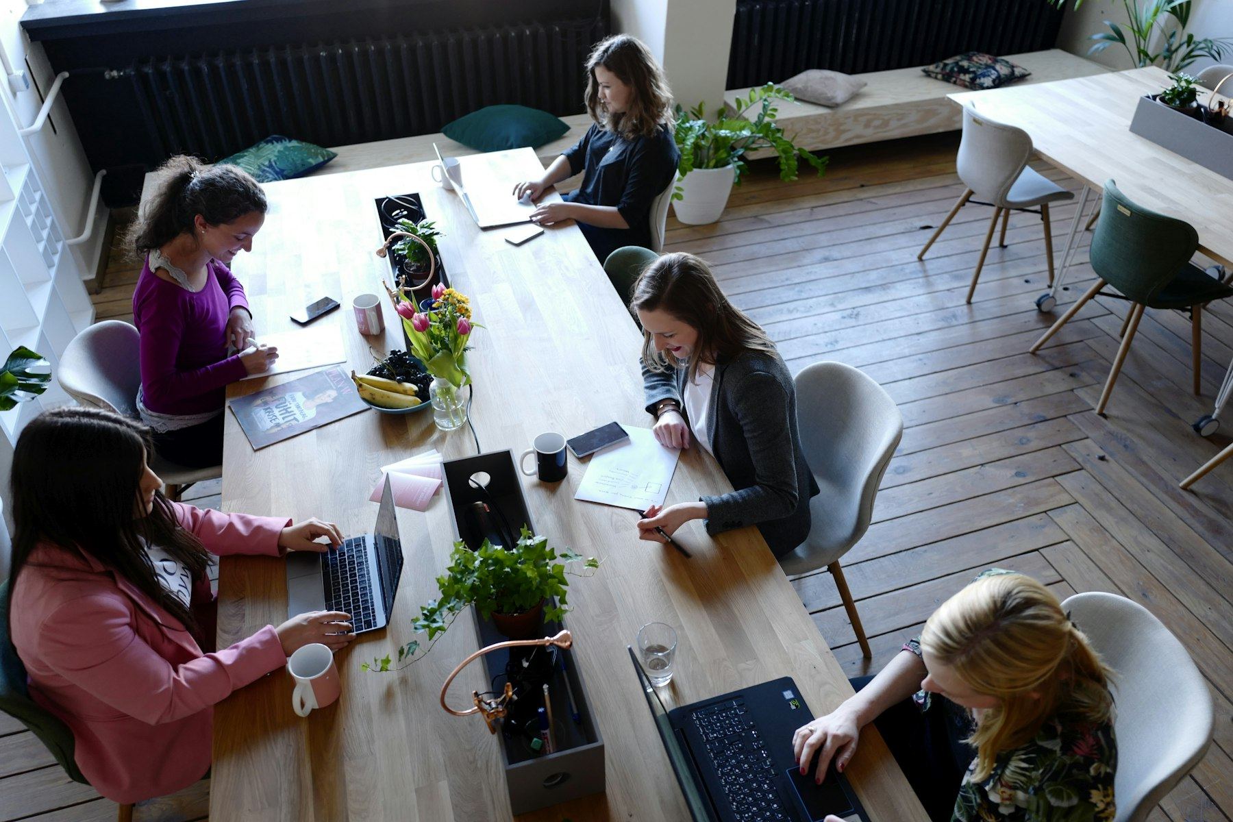 People working on laptops around a wooden table in a bright room